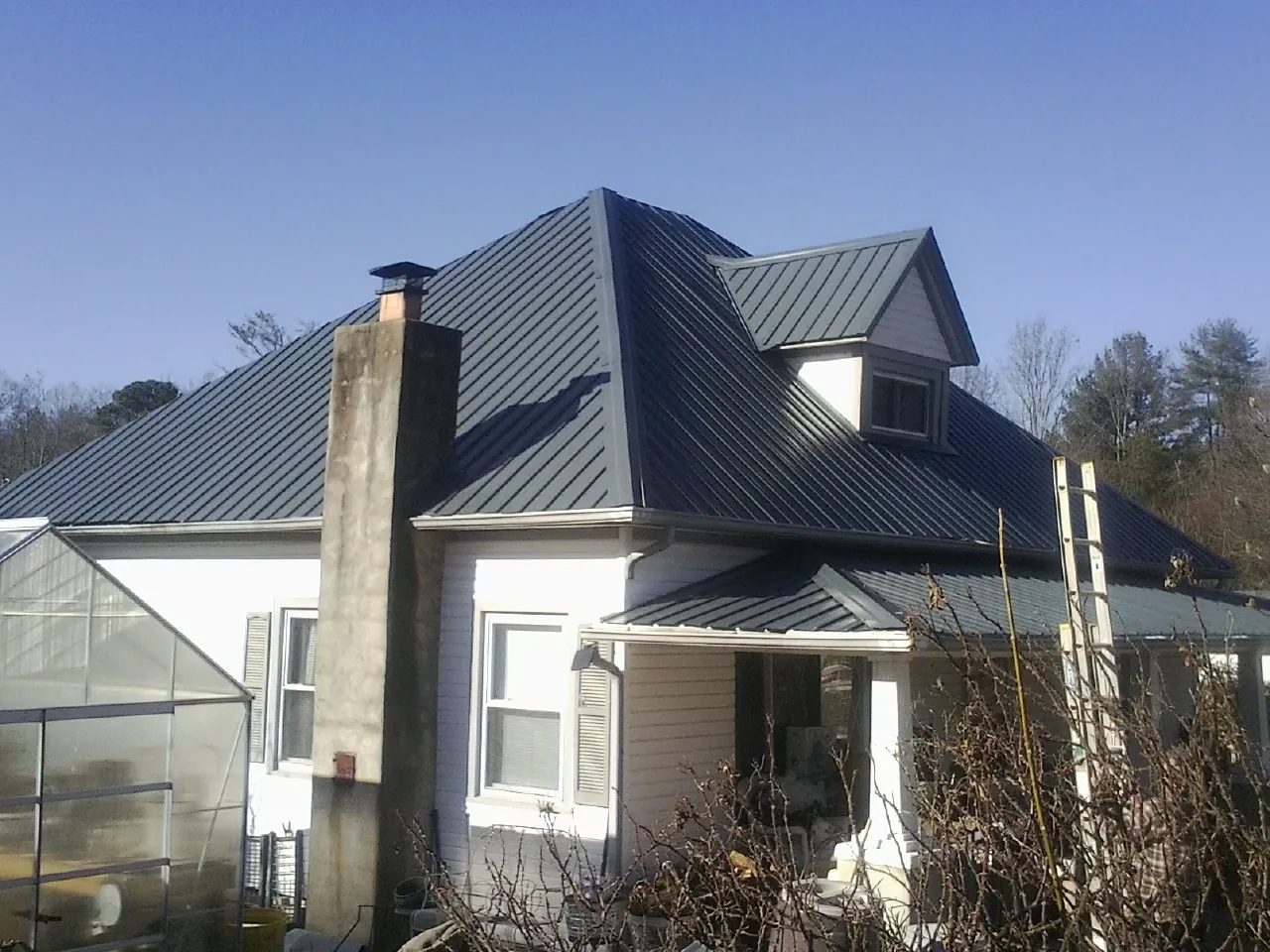 Dark blue standing seam metal roof on a white farmhouse with dormer — Slate & Tile Roof Repair by Roofing Brothers in El Campo