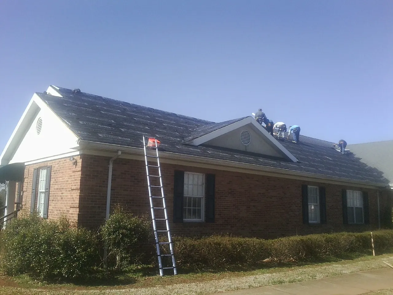 Crew tearing shingles off a brick ranch roof with a ladder set — Emergency Roof Repair work by our crew in El Campo