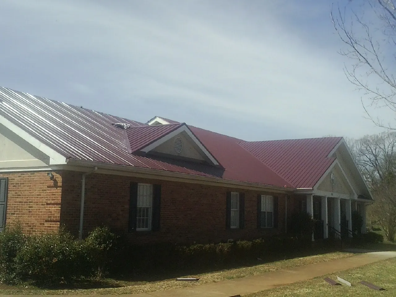 Red metal roof with gabled entries on a long brick building, from a Hail Damage Roof Repair job in El Campo
