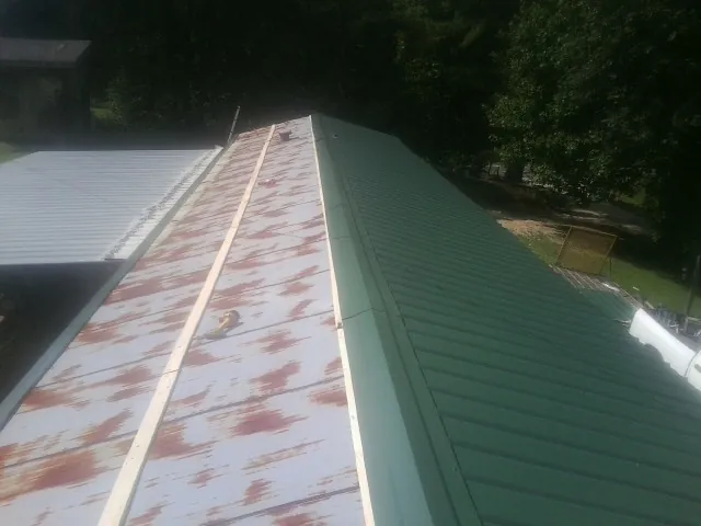 Old rusted panels beside newly installed green metal roofing — Wind Damage Roof Repair by Roofing Brothers in El Campo
