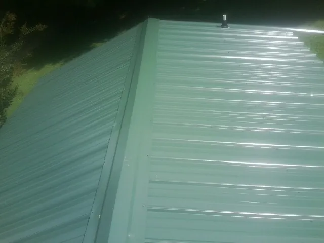 New green metal panels meeting at the ridge of a roof — Flat Roof Repair work by our crew in El Campo