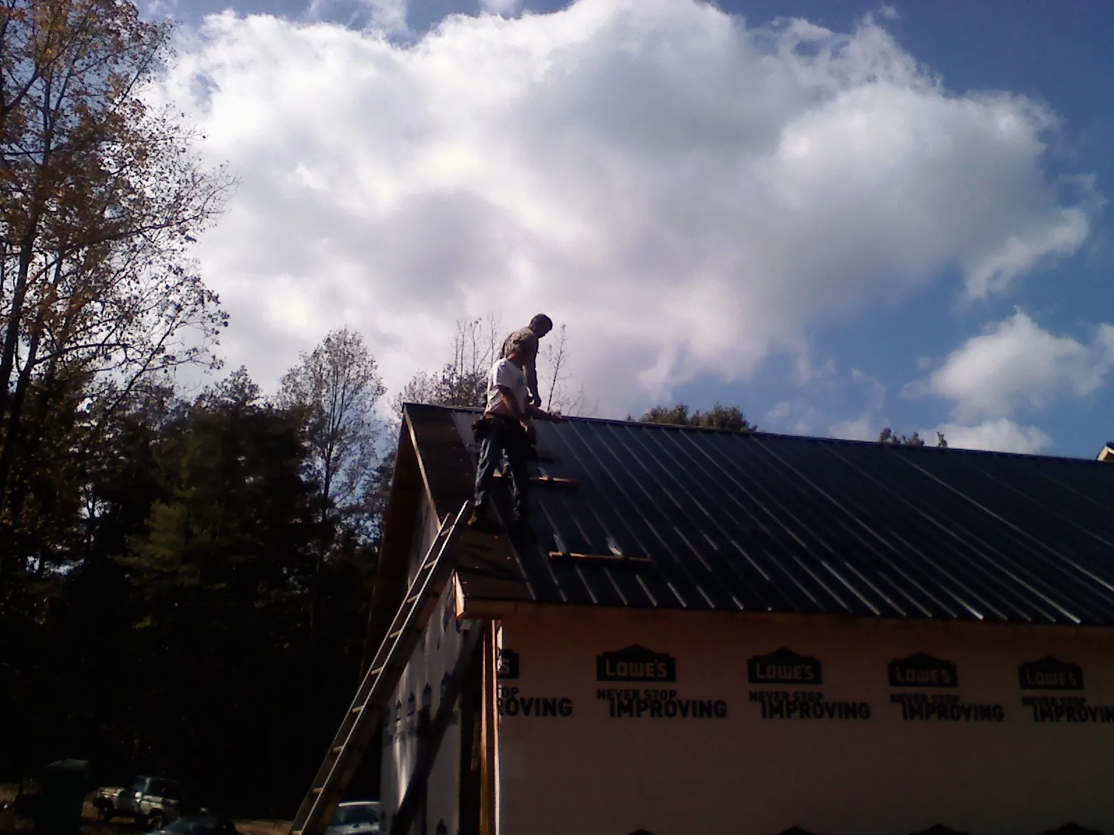 Roofer fastening dark metal panels high against a cloudy sky, from a Roof Inspection job in El Campo