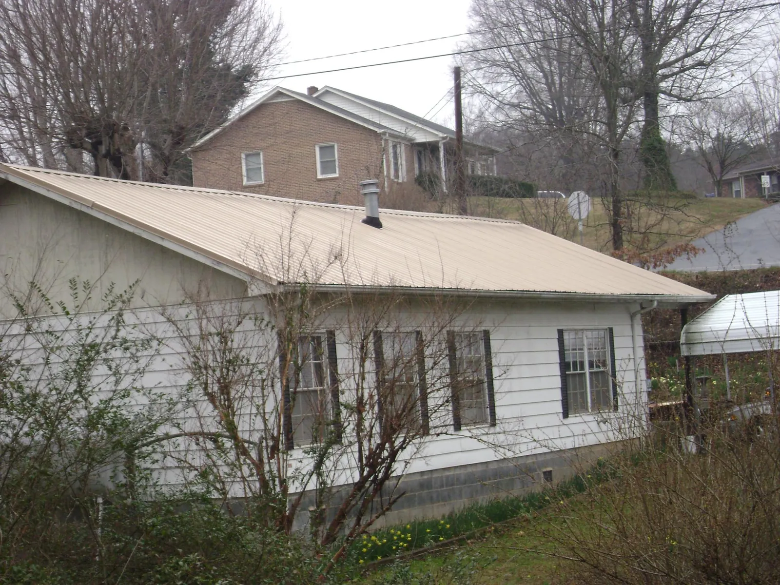 Tan metal roof on a white sided house set into a hillside — Commercial Roofing by Roofing Brothers in El Campo