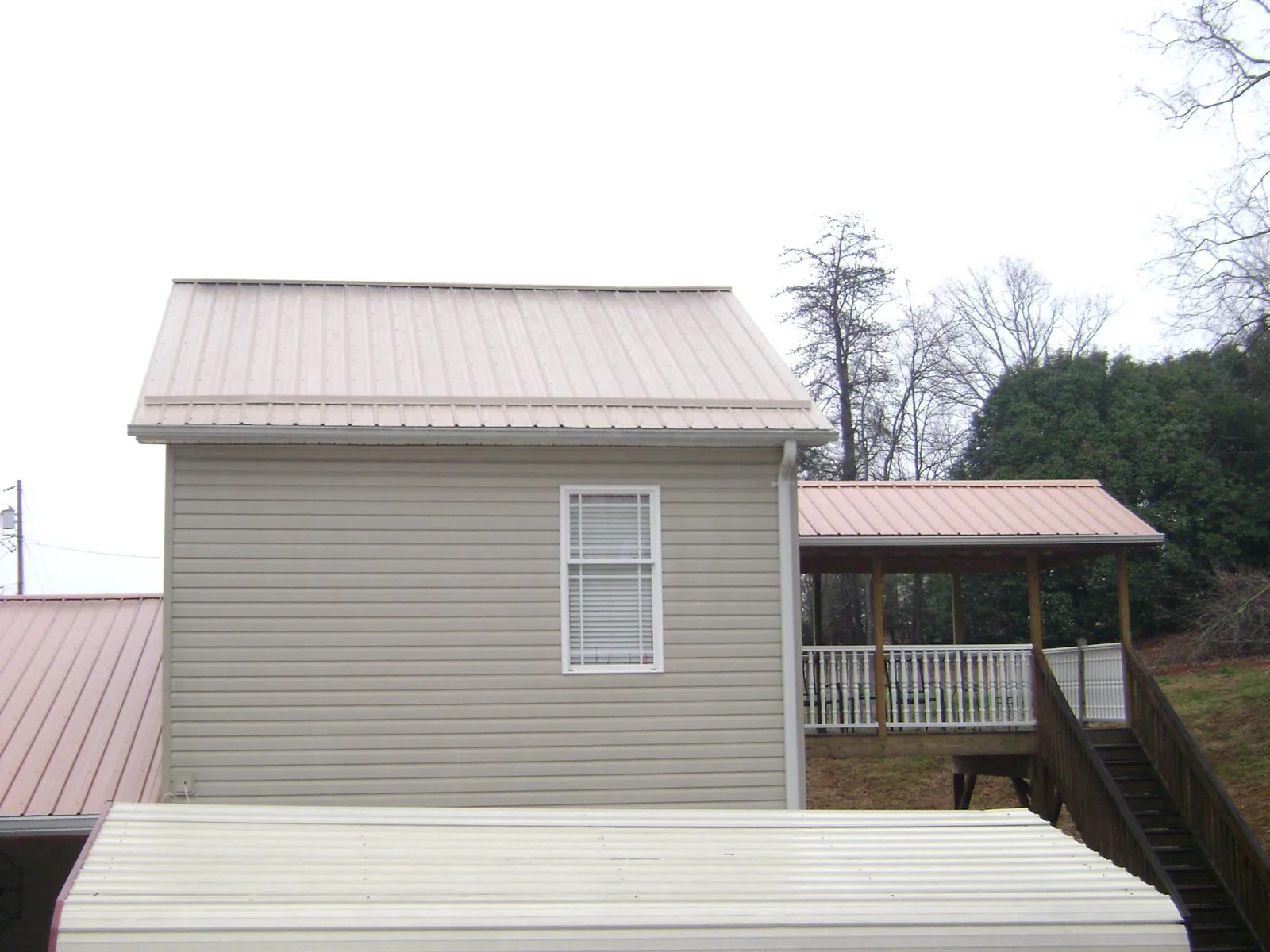 Tan metal roofs on a two story addition and attached porch, from a Roof Replacement job in El Campo